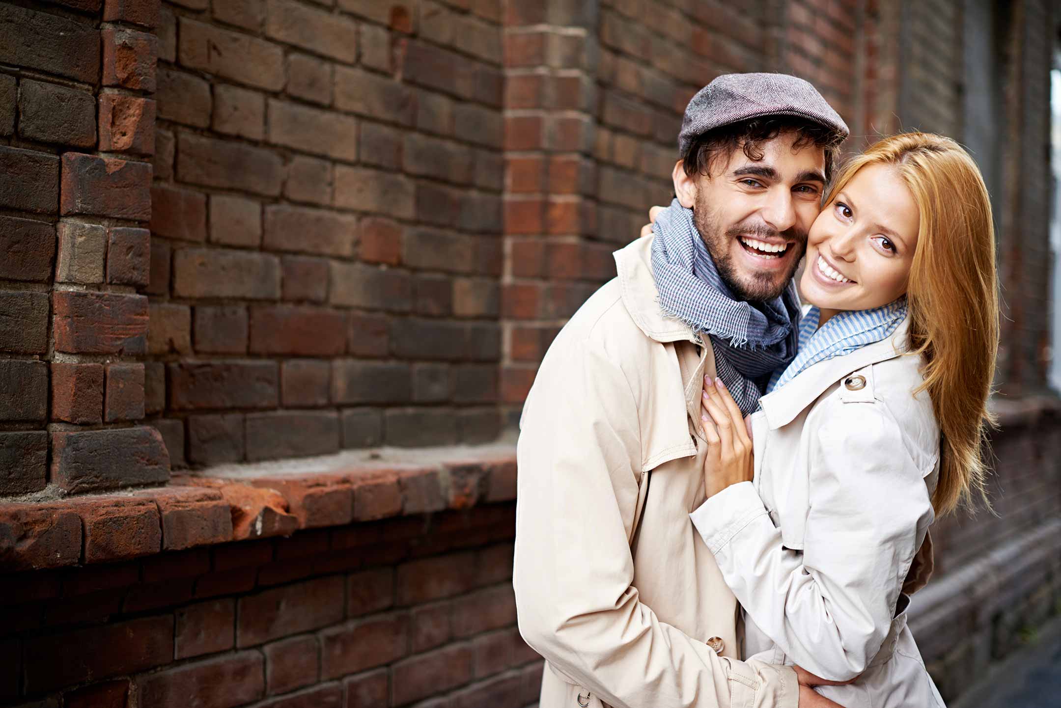 A smiling couple embracing next to a brick building.